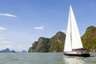 Phang Nga Körfezi 'nin turkuaz sularında ilerleyen bir yelkenli, parlak mavi gökyüzünün altındaki yüksek kireçtaşı kayalıklarıyla çevrili. Yelkenli maceraları için mükemmel koşullar..