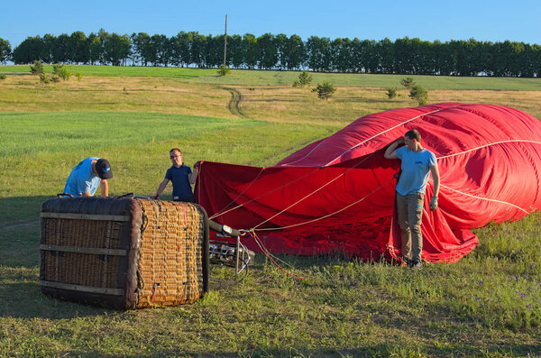 Ksaverovka, Ukraine-JUNE 06, 2018: A balloon with a basket lies on the ground, equipment for filling the balloon with cold and hot air. Flying team is preparing the balloon for launch.