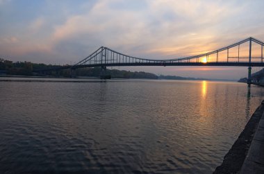 Dnipro Nehri'nin ve Yaya Köprüsü manzaralı sonbahar manzara. Güneşin suya yansıtılır. Seçici odak geniş açı lens ile. Kyiv, Ukrayna.