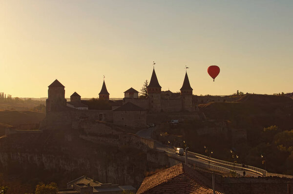 Hot air balloon flies near Kamianets-Podilskyi castle. It is famous touristic place and romantic travel destination. Beautiful autumn sunset landscape. Kamenetz Podolsky, Khmelnitsky region, Ukraine.