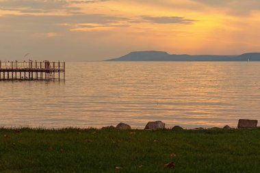 Gün batımında Balaton Gölü 'nde bir sürü kuşla iskele. Güneş suya, dağ da arka plana yansıyor. Çarpıcı sonbahar manzarası. Balatonfold, Macaristan