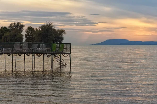 Anlegestelle mit leeren Liegestühlen am Balaton bei Sonnenuntergang. Sonne spiegelt sich im Wasser, Berg im Hintergrund. atemberaubende Herbstlandschaft. balatonfoldvar, ungarisch — Stockfoto