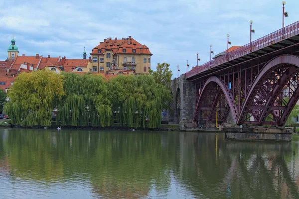 Живописное осеннее пейзажное фото города Марибор. Ошеломляющий старый мост отражается в воде реки Драва. Красивые деревья покрывают старинные здания. Марибор, Словения — стоковое фото