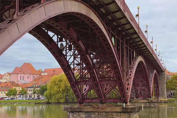 Vista de cerca de la construcción de metal del Puente Viejo en Maribor. Antiguos edificios con techos de teja roja en el fondo. Nublado día de otoño. Maribor, Eslovenia — Foto de Stock