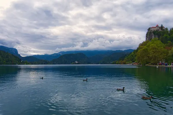 Úžasná přírodní krajina Bled Lake. Starověký hrad na vrcholku skály. Slavný ostrov s kostelem v pozadí. Na tyrkysové vodě se odrážely bouřkové mraky. Bled, Slovinsko — Stock fotografie