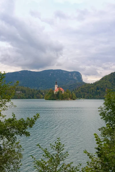 Lenyűgöző természet táj Bled-tó Szent Mária templom Nagyboldogasszony kis szigeten. Természetes keret formájában zöld levelek. Bled, Szlovénia — Stock Fotó