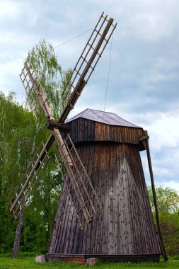 Bahar güneşli bir günde antik ahşap rüzgar değirmeninin manzarası. Arka planda güzel yaşlı ağaçlar var. Seyahat ve turizm konsepti. Antik Ukrayna 'nın tarihi binaları kavramı.