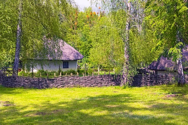 茅葺き屋根の下にある古代の粘土の家の絵のような風景で 晴れた日には庭がウィッカーフェンスに囲まれています 古代ウクライナの歴史的建造物の概念 — ストック写真