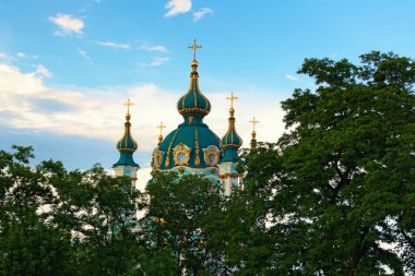 Antik St. Andrew Kilisesi 'nin kubbeleri beyaz bulutlu mavi gökyüzüne karşı. Ağaç Yaprakları Sınırı. Doğal Çerçeve. Güneşli bir yaz günü. Kyiv, Ukrayna. 