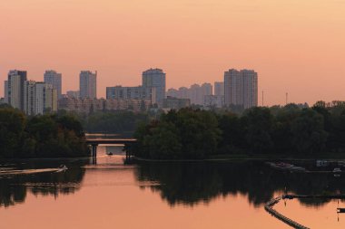 Kyiv 'de sonbaharın muhteşem sabah manzarası. Dnipro Nehri 'nin sularına yansıyan ağaçlar. İlk küçük balıkçı tekneleri balığa gidiyor. Arka planda modern gökdelenler var. Kyiv, Ukrayna.