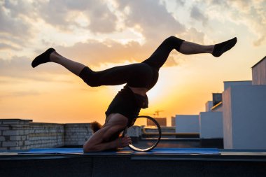 Orta yaşlı bir adam yogada tekerlek kullanmakla meşgul. Gün batımında çatıda yoga..