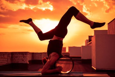 Orta yaşlı bir adam yogada tekerlek kullanmakla meşgul. Gün batımında çatıda yoga..