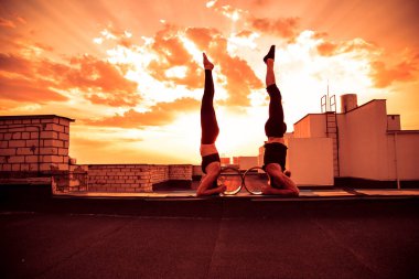 Bir erkek ve bir kadın buhar yogası yapıyorlar. Gün batımında çatıda yoga..