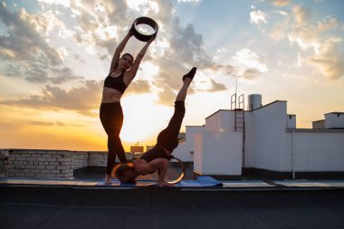 Bir erkek ve bir kadın buhar yogası yapıyorlar. Gün batımında çatıda yoga..