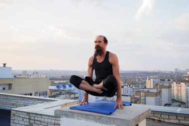 Orta yaşlı bir adam çatıda yoga yapıyor. Gün batımında çatıda yoga..