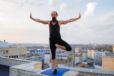 Orta yaşlı bir adam çatıda yoga yapıyor. Gün batımında çatıda yoga..