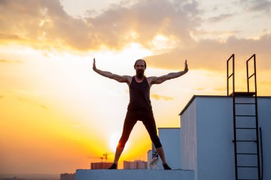 Orta yaşlı bir adam çatıda yoga yapıyor. Gün batımında çatıda yoga..