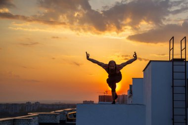 Orta yaşlı bir adam çatıda yoga yapıyor. Gün batımında çatıda yoga..