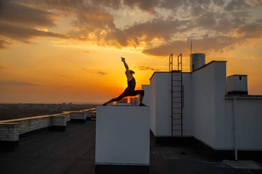 Orta yaşlı bir adam çatıda yoga yapıyor. Gün batımında çatıda yoga..