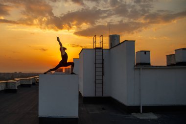 Orta yaşlı bir adam çatıda yoga yapıyor. Gün batımında çatıda yoga..