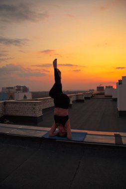 Orta yaşlı bir kadın yoga yapıyor. Gün batımında çatıda yoga.