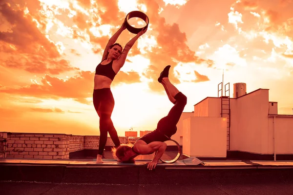 Bir erkek ve bir kadın buhar yogası yapıyorlar. Gün batımında çatıda yoga..