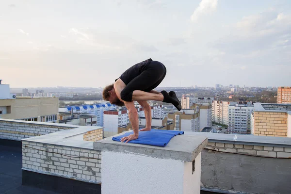 Orta yaşlı bir adam çatıda yoga yapıyor. Gün batımında çatıda yoga..