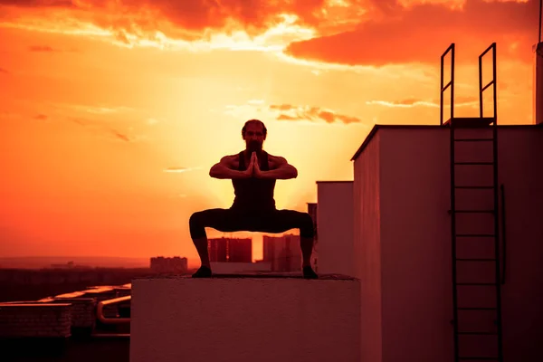 A middle-aged man is engaged in yoga on the roof. Yoga on the roof at sunset.
