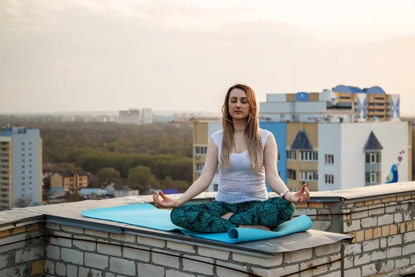 Genç beyaz kadın çatıda meditasyon yapıyor. Gün batımında çatıda yoga..