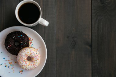 Siyah kahve beyaz kupa ve bir plaka üzerinde iki çikolata. Ahşap bir masaya. Yukarıdan görüntülemek