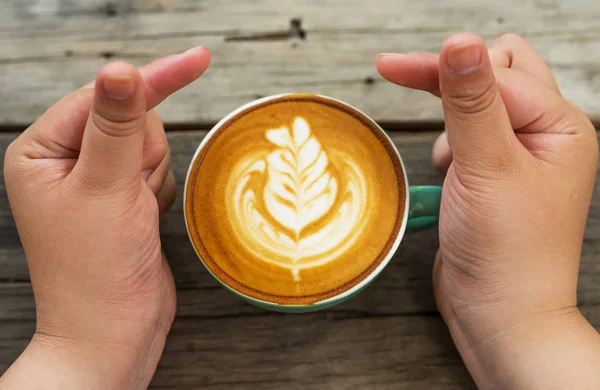 Hand women with cappuccino coffee in a green cup on wooden blurred background