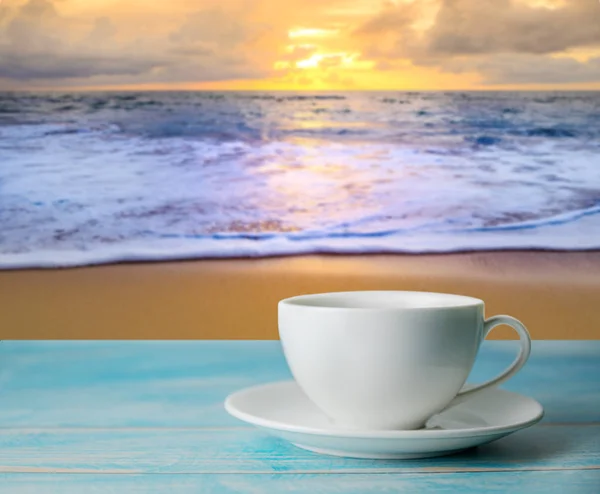 A cup of coffee with blurred beach sunset or sunrise and colorfu