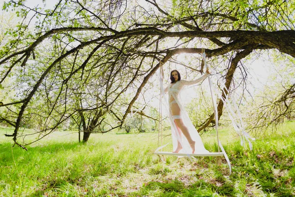 Verleidelijke jonge bruid in witte lingerie poseren op een schommel — Stockfoto