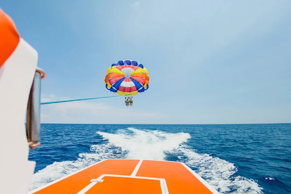 Gente volando en un colorido paracaídas remolcado por un barco a motor — Foto de Stock