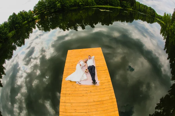 Couple de jeunes mariés et la surface du lac avec réflexion du ciel nuageux — Photo