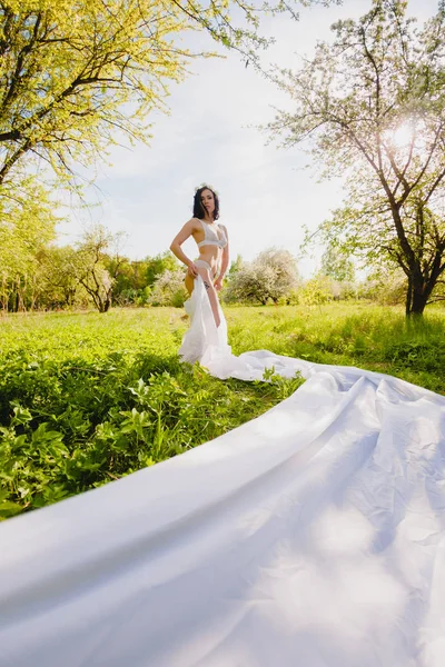 Jeune brune sexy posant dans un jardin fleuri avec un long morceau de tissu blanc — Photo