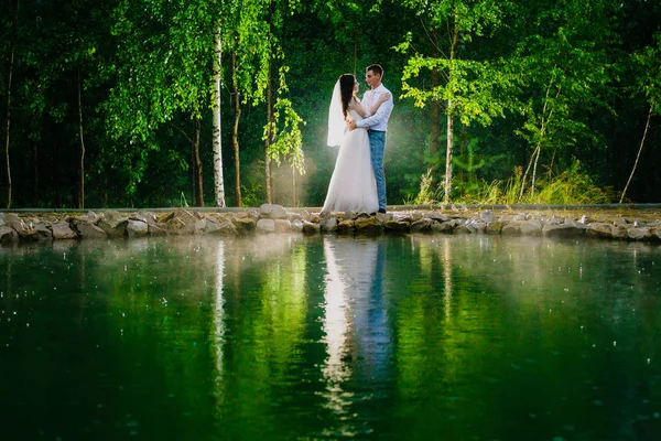 Brautpaar steht neben einem Teich im Regen — Stockfoto