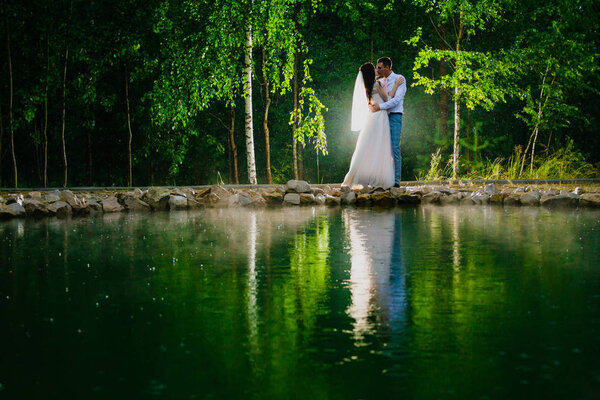 Newlywed couple standing next to a pond in the rain