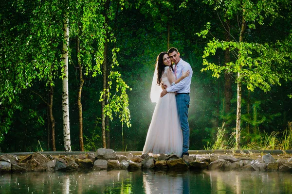 Couple nouvellement marié debout à côté d'un étang sous la pluie — Photo