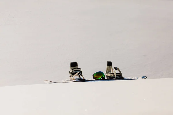 Snowboard e ski googles adagiati su una neve vicino alla pista freeride — Foto Stock