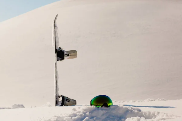 Сноуборд і лижні окуляри лежать на снігу біля схилу фрірайду — стокове фото