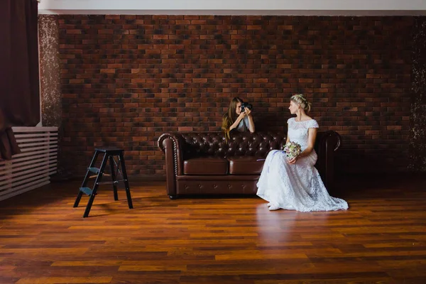 Fotograaf fotograferen de bruid in de studio op een grote lederen sofa — Stockfoto