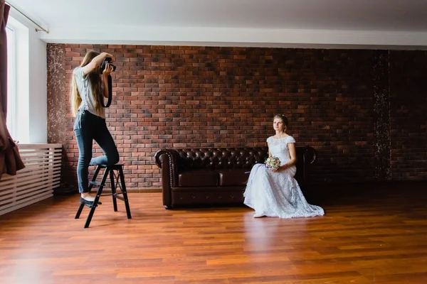 Fotograf fotí nevěsta v ateliéru na velká kožená pohovka — Stock fotografie