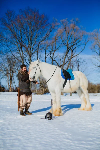 Homem de terno de guerreiro antigo que está perto do grande cavalo branco — Fotografia de Stock