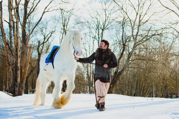 Homem de terno de guerreiro antigo andando com o grande cavalo branco — Fotografia de Stock