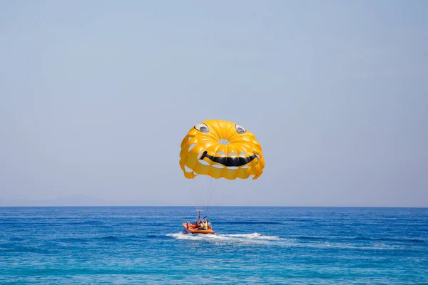 Ein paar Touristen fliegen an einem gelben Fallschirm mit einem lächelnden Gesicht darauf — Stockfoto