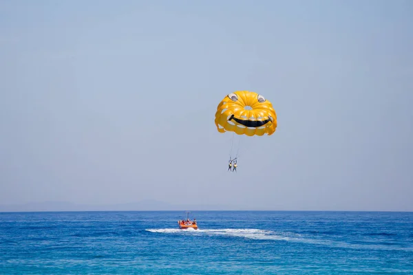 Пара туристів літає на жовтому парашуті з усміхненим обличчям на ньому — стокове фото