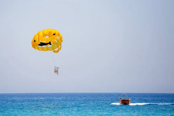 Three tourists flying on a yellow parachute with smiling face on it — Stock Photo, Image
