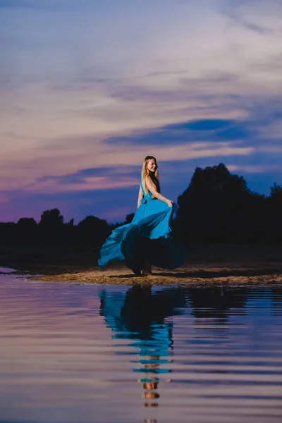 Piękny blond model w niebieskiej sukni powietrza stwarzające tuż przy brzegu morza — Zdjęcie stockowe