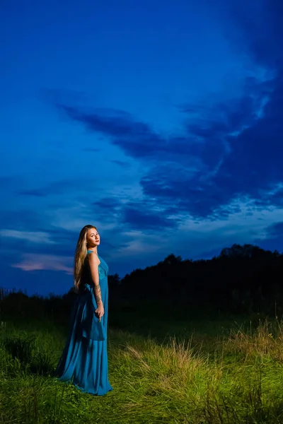 Красивая блондинка в синем воздушном платье позирует на зеленом лугу — стоковое фото